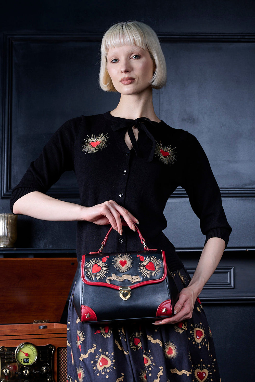 Woman holding a black handbag with red accents against a dark background