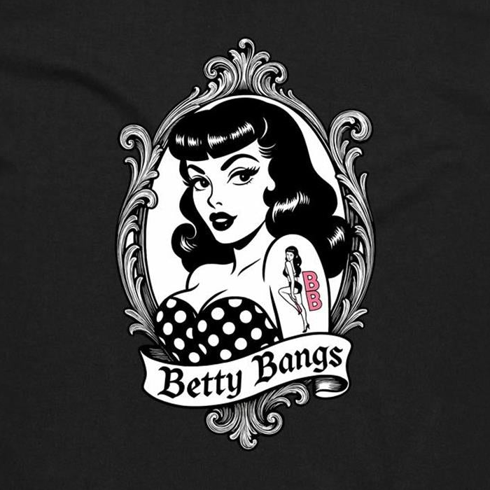 A black t-shirt featuring a vintage-style pin-up graphic of a woman with wavy black hair, a polka-dot top, and a tattoo reading 'BBB' on her arm, framed by an ornate silver border with a banner below reading 'Betty Bangs'.