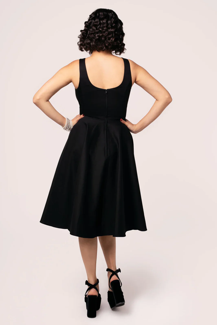 Person wearing a black dress with hands on hips against a white background