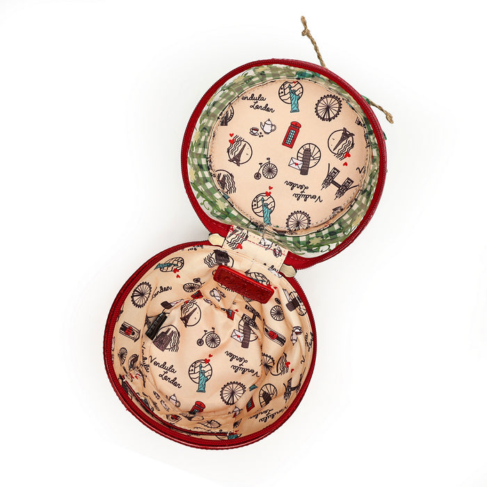 An open round velvet jewelry box with a red velvet exterior and a vintage London-themed printed interior featuring red double-decker buses, bicycles, and the word 'Victoria'.