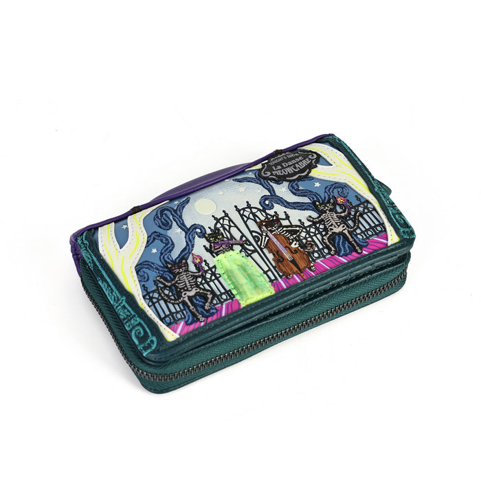 A small zip-around wallet with a dark teal-green base and a colorful printed illustration on the front. The artwork shows a spooky graveyard scene with skeletons, a casket, and swirling blue and pink clouds.