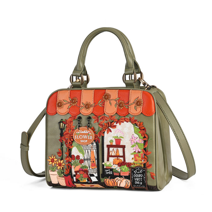 An olive green handbag with a detailed autumn-themed floral shop illustration on the front, featuring orange awnings, pumpkins, flowers, and a storefront scene, shown on a white background.