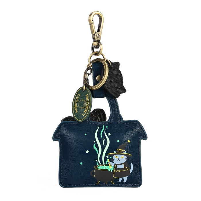 A dark blue house-shaped leather keychain bag featuring a cartoon cat in a wizard hat next to a cauldron with green steam. The bag is attached to a gold-tone lobster clasp, key ring, and a round 'The Cat Company' brand tag.