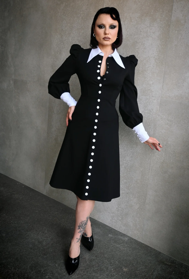 Woman wearing a black dress with white buttons against a gray background