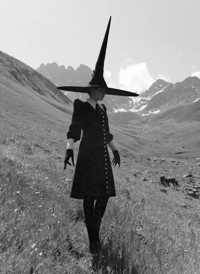 Person wearing a large witch hat in a mountainous landscape