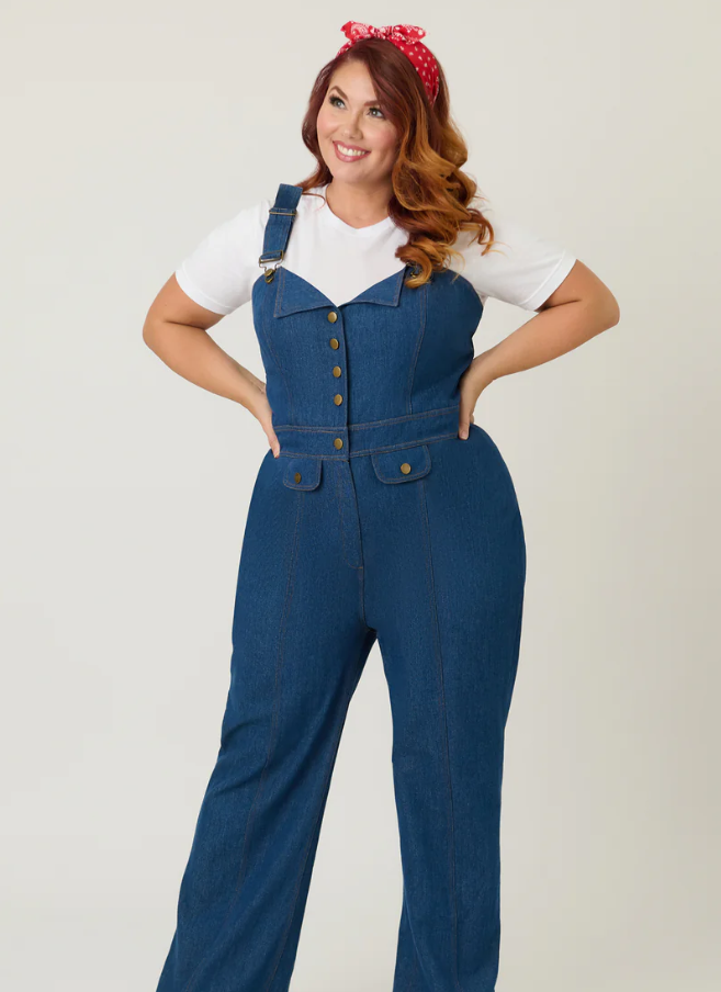 Woman wearing blue denim overalls with a white shirt on a plain background