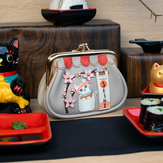 Handbag with cat design and 'Sushi' text on a decorative table with cat figurines and sushi models.
