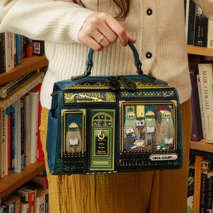 Person holding a decorative handbag with book-themed design in a library setting