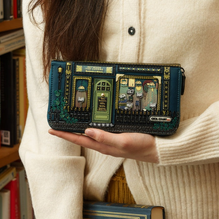 Person holding a decorative wallet with a book-themed design, surrounded by books.