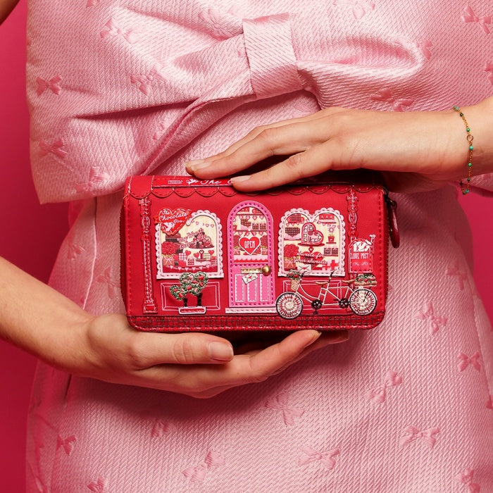 Red patterned wallet held by hands against a pink background