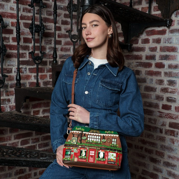 Woman holding a decorative bag with a house design against a brick wall.
