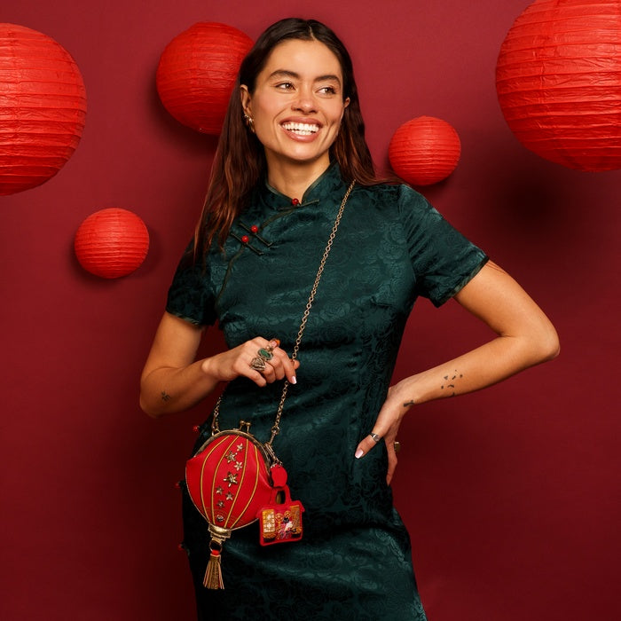 Woman in a dark green dress holding a red lantern against a red background with red lanterns.