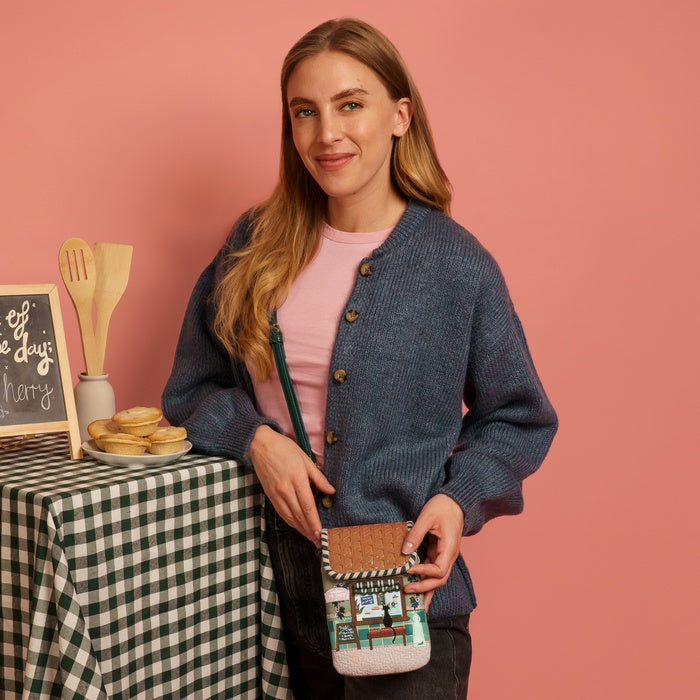 Woman holding a patterned handbag in front of a table with baking items on a pink background