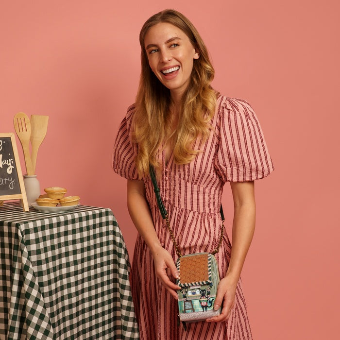 Woman in a pink checkered dress holding a small handbag with a pink background