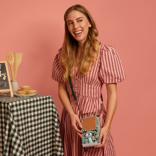 Woman in a pink checkered dress holding a small handbag with a pink background