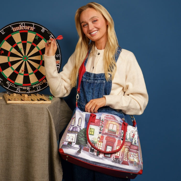 Woman holding a colorful bag with a building design, standing next to a dartboard.