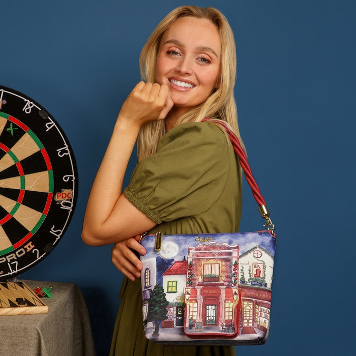 Woman holding a colorful handbag with a building design, standing next to a dartboard on a blue background