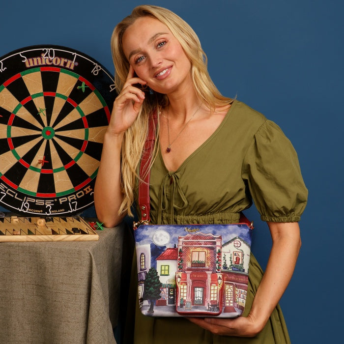 Woman holding a handbag with a colorful design in front of a dartboard.