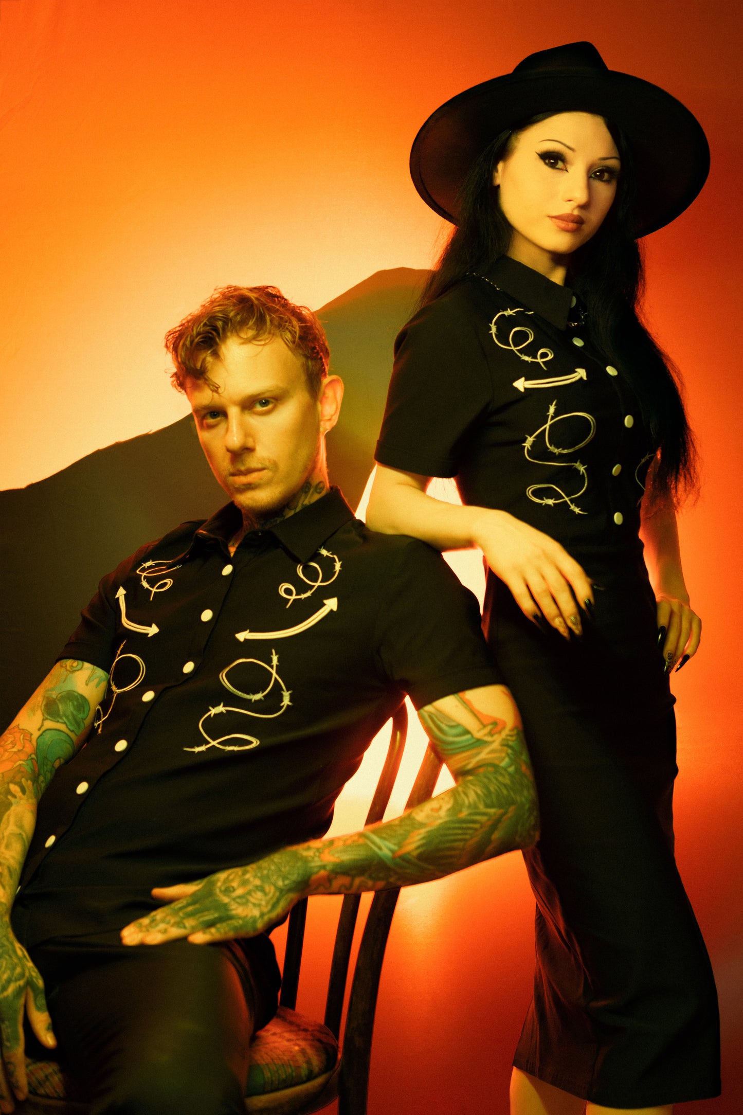 Two people wearing black outfits with white designs against a warm-toned background
