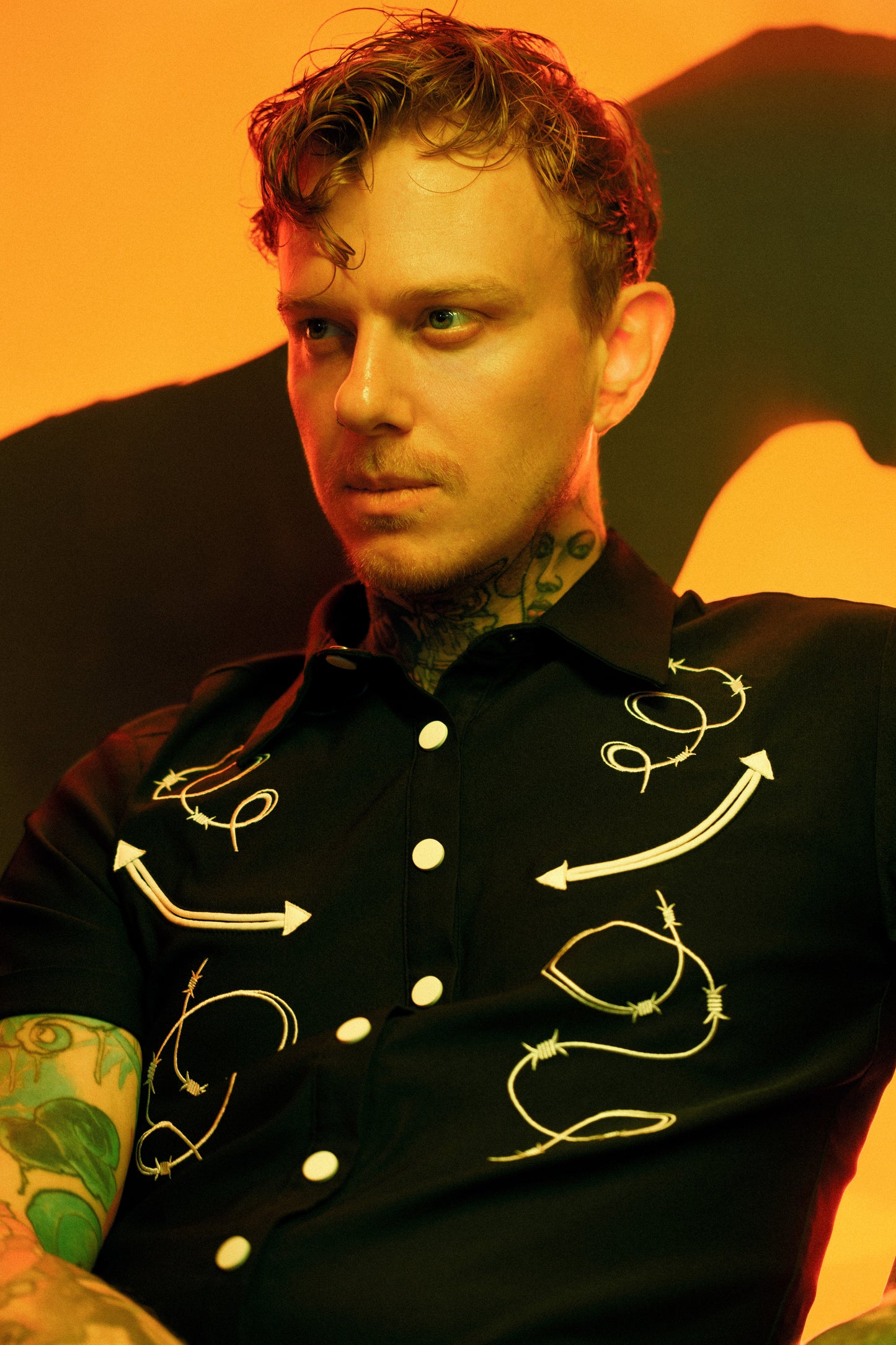 Man wearing a black shirt with white embroidery against an orange background
