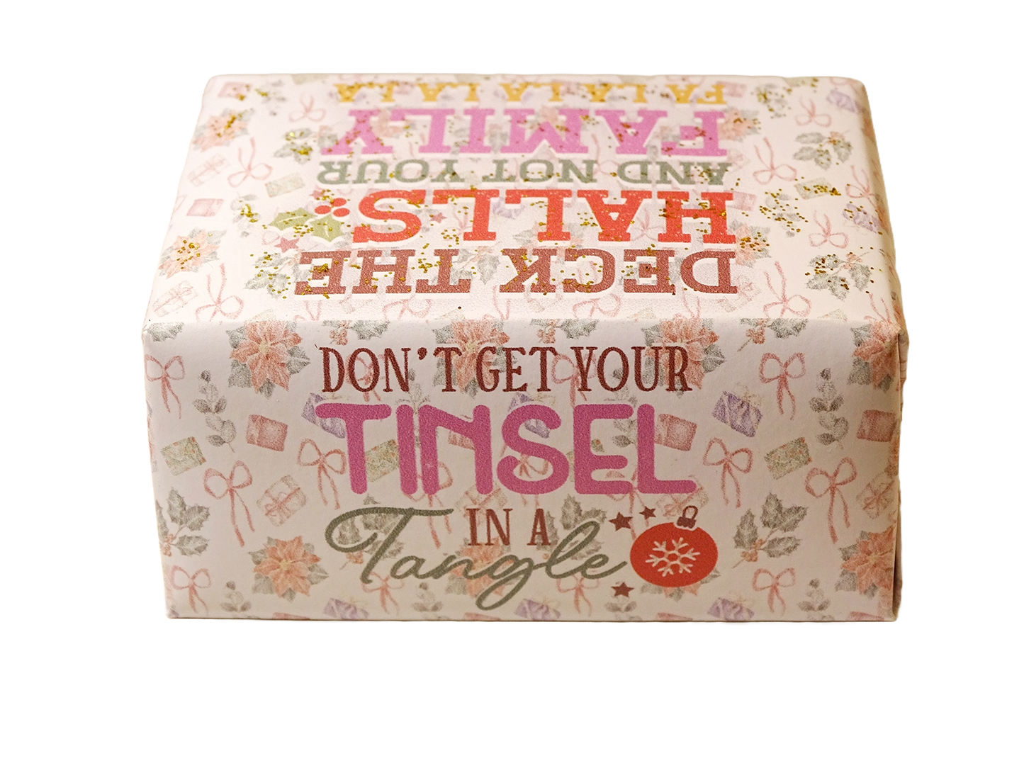 A square decorative box with a festive holiday design, featuring the text 'DON'T GET YOUR TINSEL IN A TANGLE' and 'DECK THE HALLS AND NOT YOUR FAMILY' in pink, red, and green lettering on a cream background with floral and gift motifs.