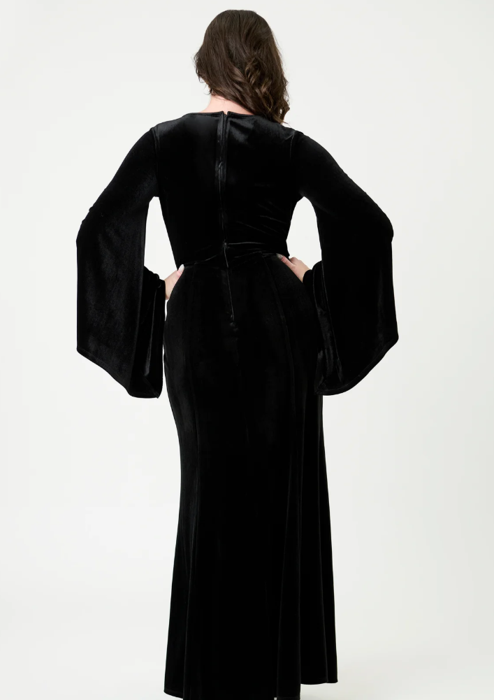 Person wearing a black velvet dress with wide sleeves on a white background