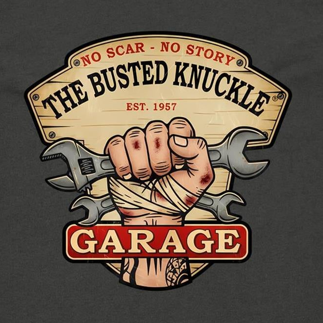 A graphic print on a dark charcoal t-shirt featuring a vintage-style sign that reads 'THE BUSTED KNUCKLE GARAGE' with a bandaged hand and crossed wrenches in the center.