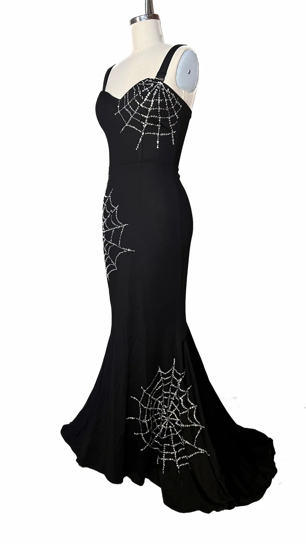 Black evening gown with spider web embellishments on a mannequin against a white background