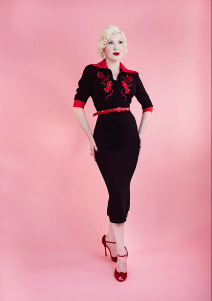 Woman wearing a black dress with red accents on a pink background