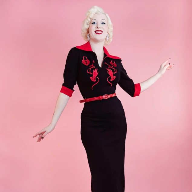 Woman wearing a black dress with red accents against a pink background