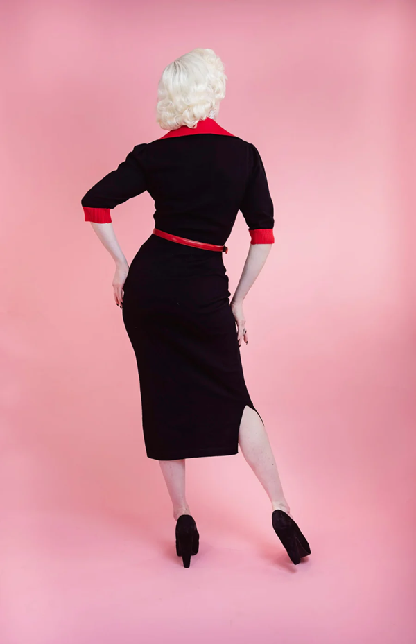 Person wearing a black dress with red accents against a pink background