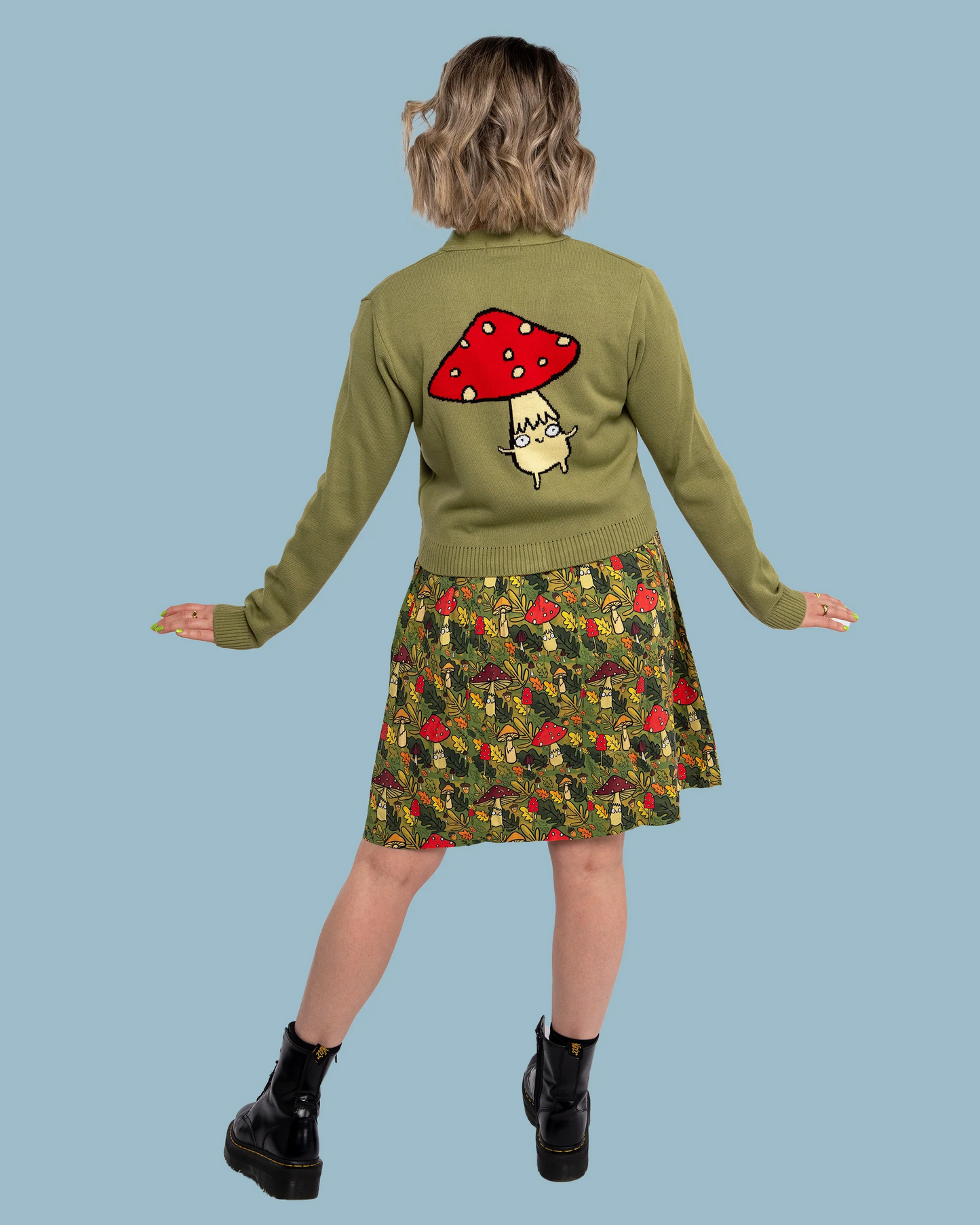 Person wearing a green sweater with a mushroom design and a patterned skirt on a blue background