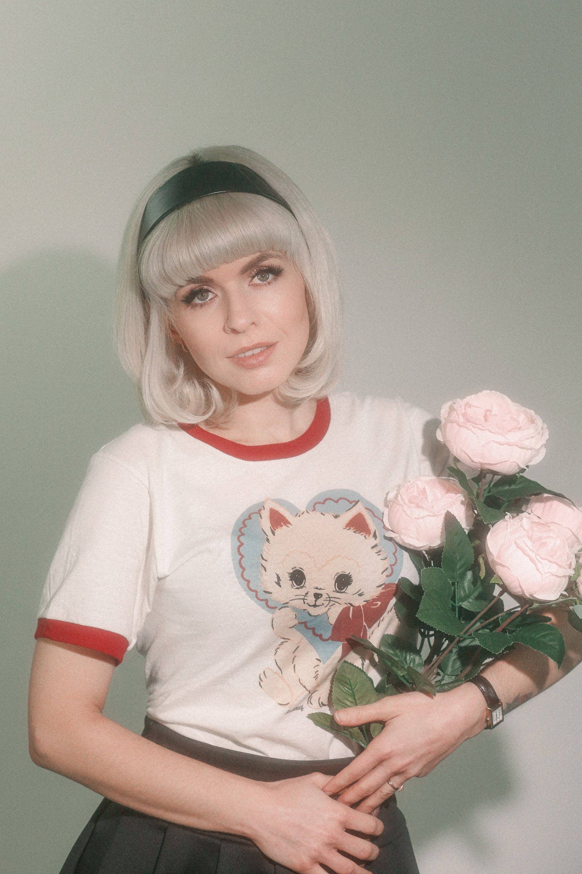 Person wearing a t-shirt with a cat graphic and holding flowers against a plain background