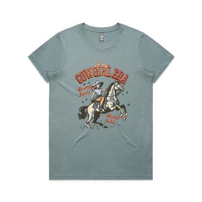 A white graphic t-shirt featuring a retro western illustration of a cowgirl riding a horse. The text reads 'In my COWGIRL ERA' in arched red letters, 'Always Sassy' in red script, and 'Always Wild' in red script, with the cowgirl wearing a cowboy hat and boots while riding a rearing horse.