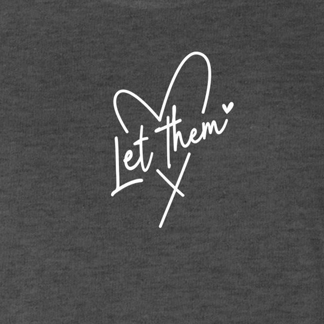 A close-up of a dark heather gray fabric with a white cursive graphic reading 'Let them' integrated with a heart and cross design.