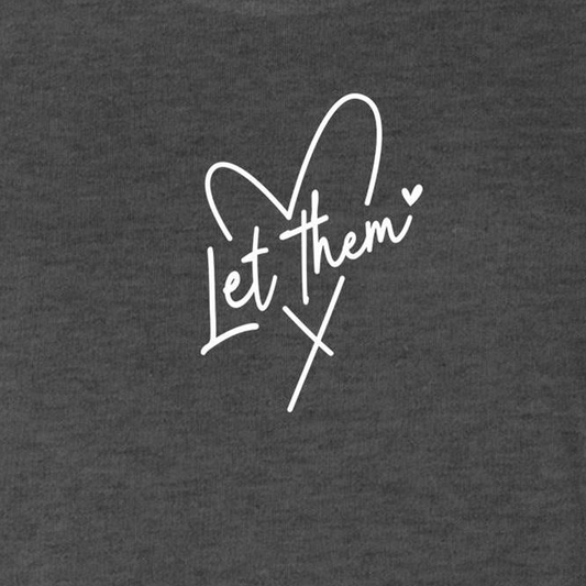 A close-up of a dark heather gray fabric with a white cursive graphic reading 'Let them' integrated with a heart and cross design.