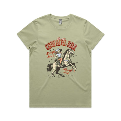 A white graphic t-shirt featuring a retro western illustration of a cowgirl riding a horse. The text reads 'In my COWGIRL ERA' in arched red letters, 'Always Sassy' in red script, and 'Always Wild' in red script, with the cowgirl wearing a cowboy hat and boots while riding a rearing horse.