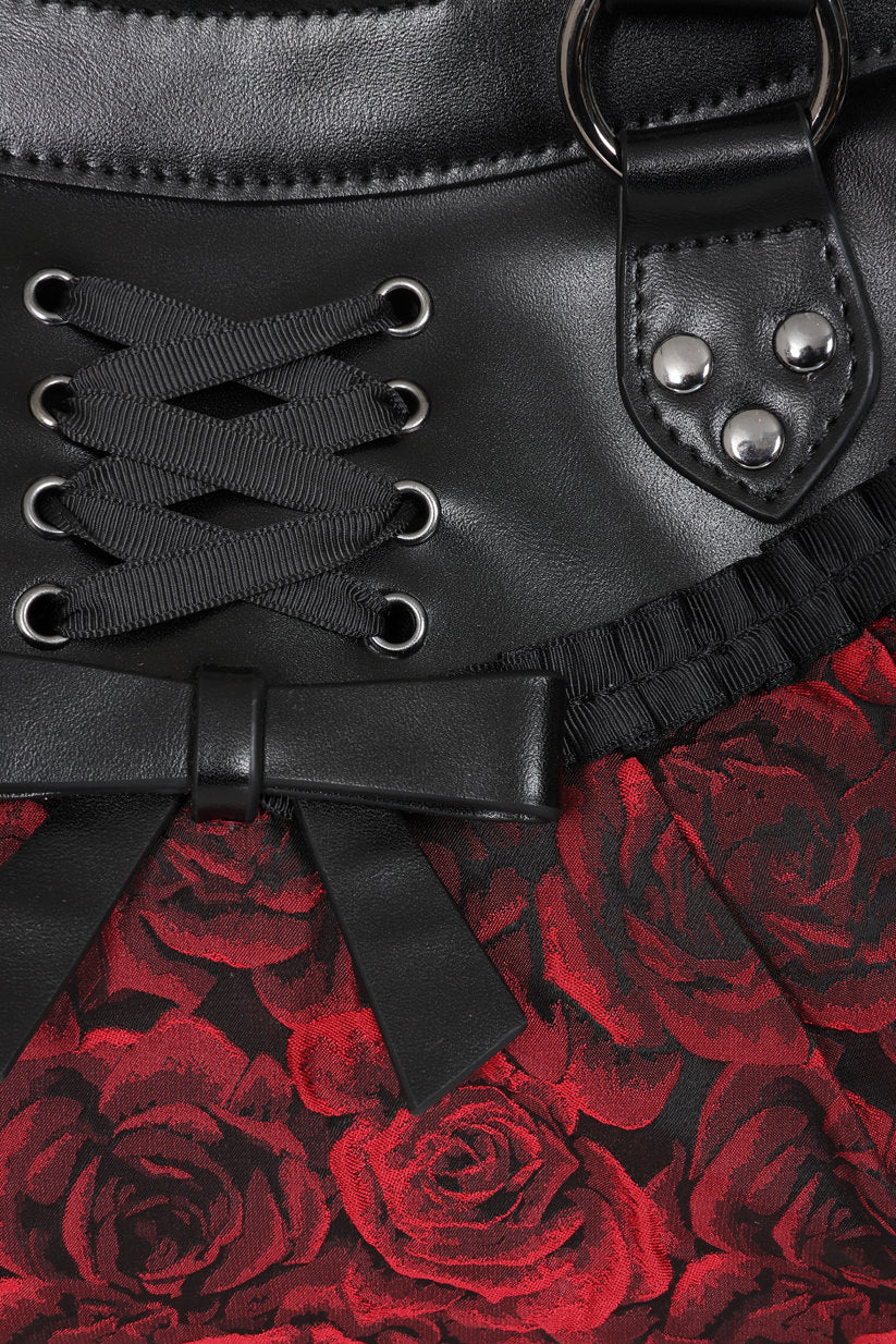 Close-up of a black faux-leather corset-style waistband with lace-up front, metal eyelets, silver studs, and a red rose patterned fabric below.