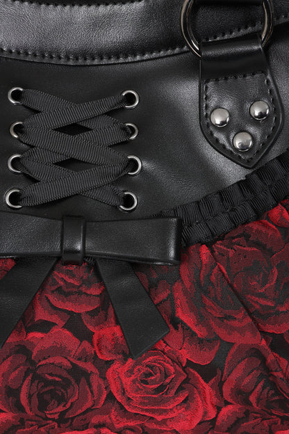 Close-up of a black faux-leather corset-style waistband with lace-up front, metal eyelets, silver studs, and a red rose patterned fabric below.