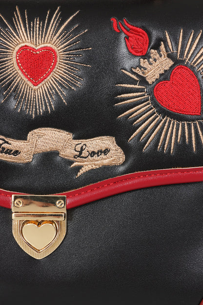 Close-up of a black leather handbag featuring red and beige embroidered heart and flame motifs, a red band, and a gold heart-shaped clasp.
