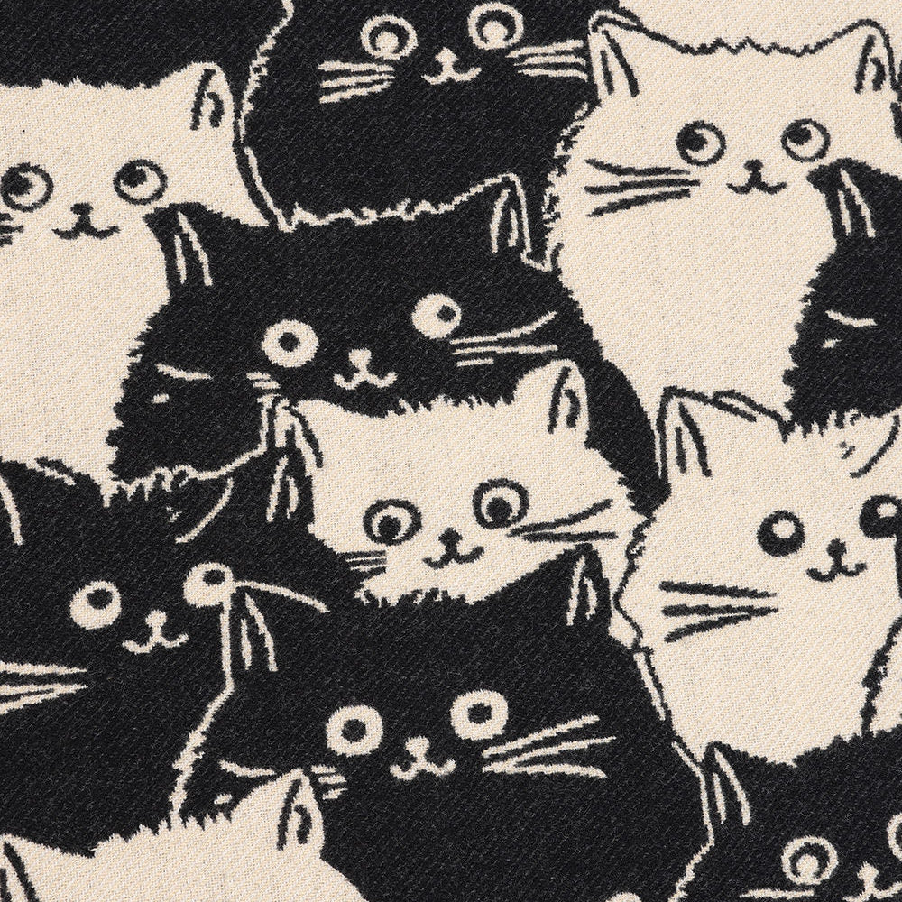 A close-up of a fabric pattern featuring cartoon-style black and white cat faces on a warm off-white background.