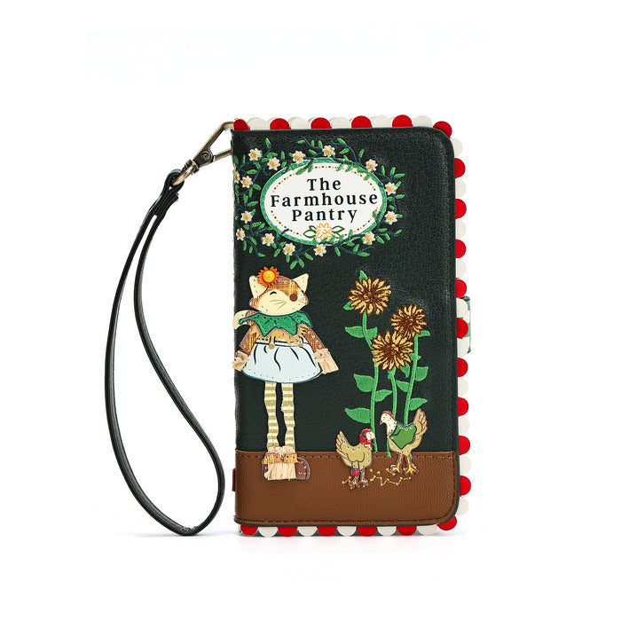 A black faux-leather wallet with a wrist strap, decorated with a whimsical 'The Farmhouse Pantry' illustration featuring a cat, flowers, sunflowers, chickens, and a brown base, finished with red and white pom-pom trim.
