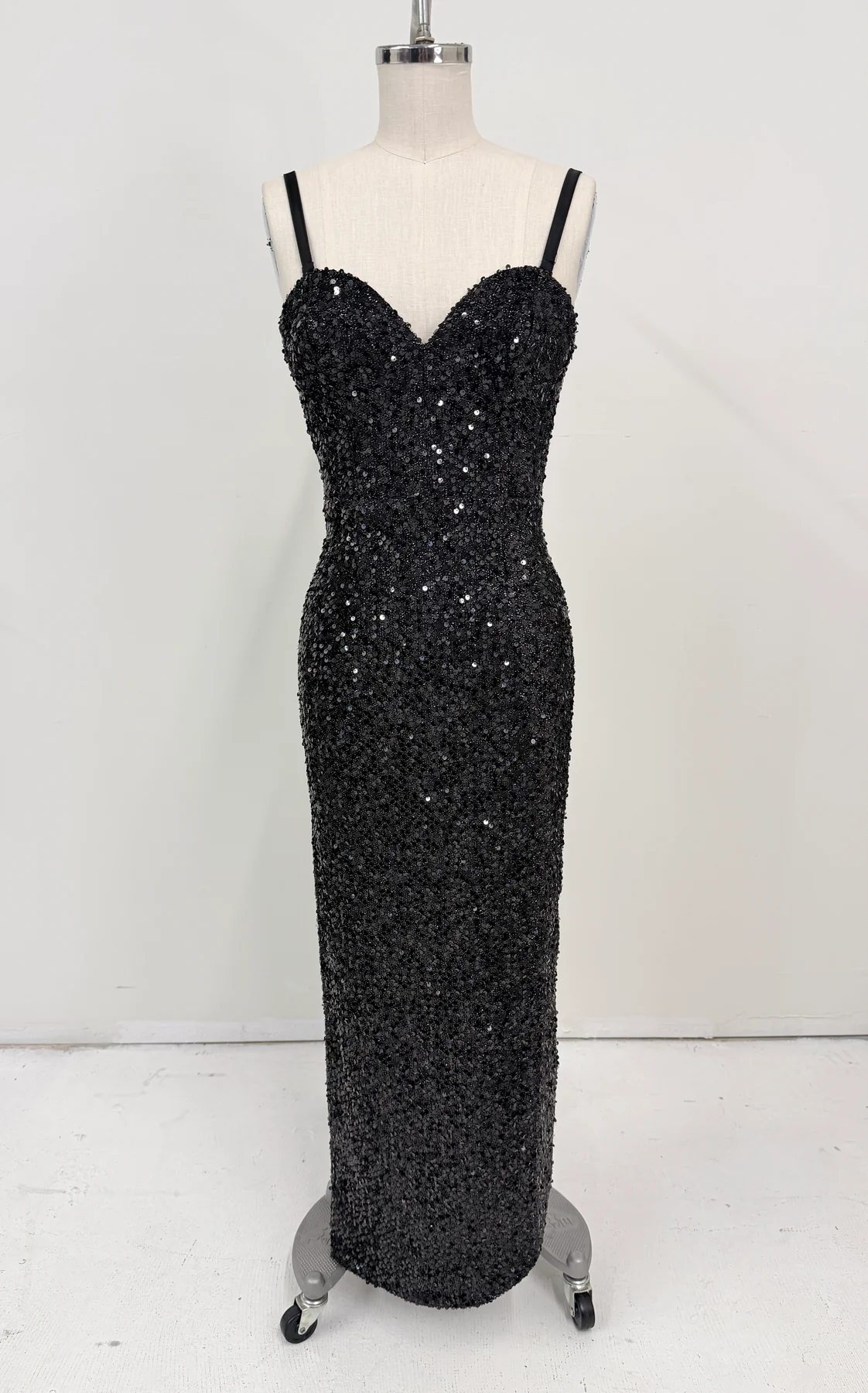 A black sequined evening gown with thin spaghetti straps and a sweetheart neckline, displayed on a headless mannequin dress form against a plain white studio background.