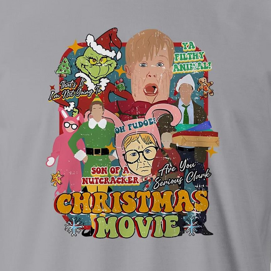 A close-up of a gray fabric garment featuring a large, colorful graphic print on the front. The print is a collage of characters and text from the movie 'Son of a Nutcracker: Are You Serious, Clerk?' including the Grinch in Santa hat, a blonde boy, a woman in a green dress, and bold text reading 'CHRISTMAS MOVIE'.