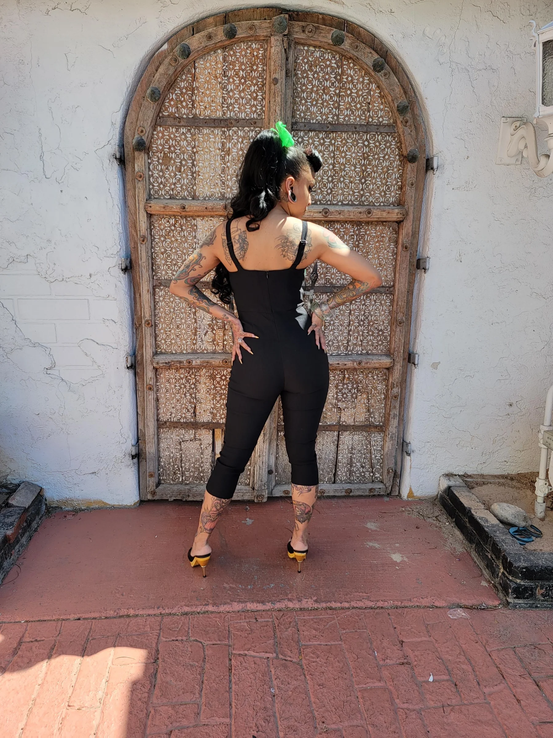 Person wearing a black outfit with tattoos standing in front of an ornate wooden door.