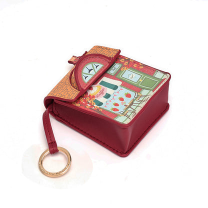 A small red leather key case with a decorative printed flap featuring a strawberry-themed illustration, a clock detail, and a gold-tone key ring attached, shown on a white background.