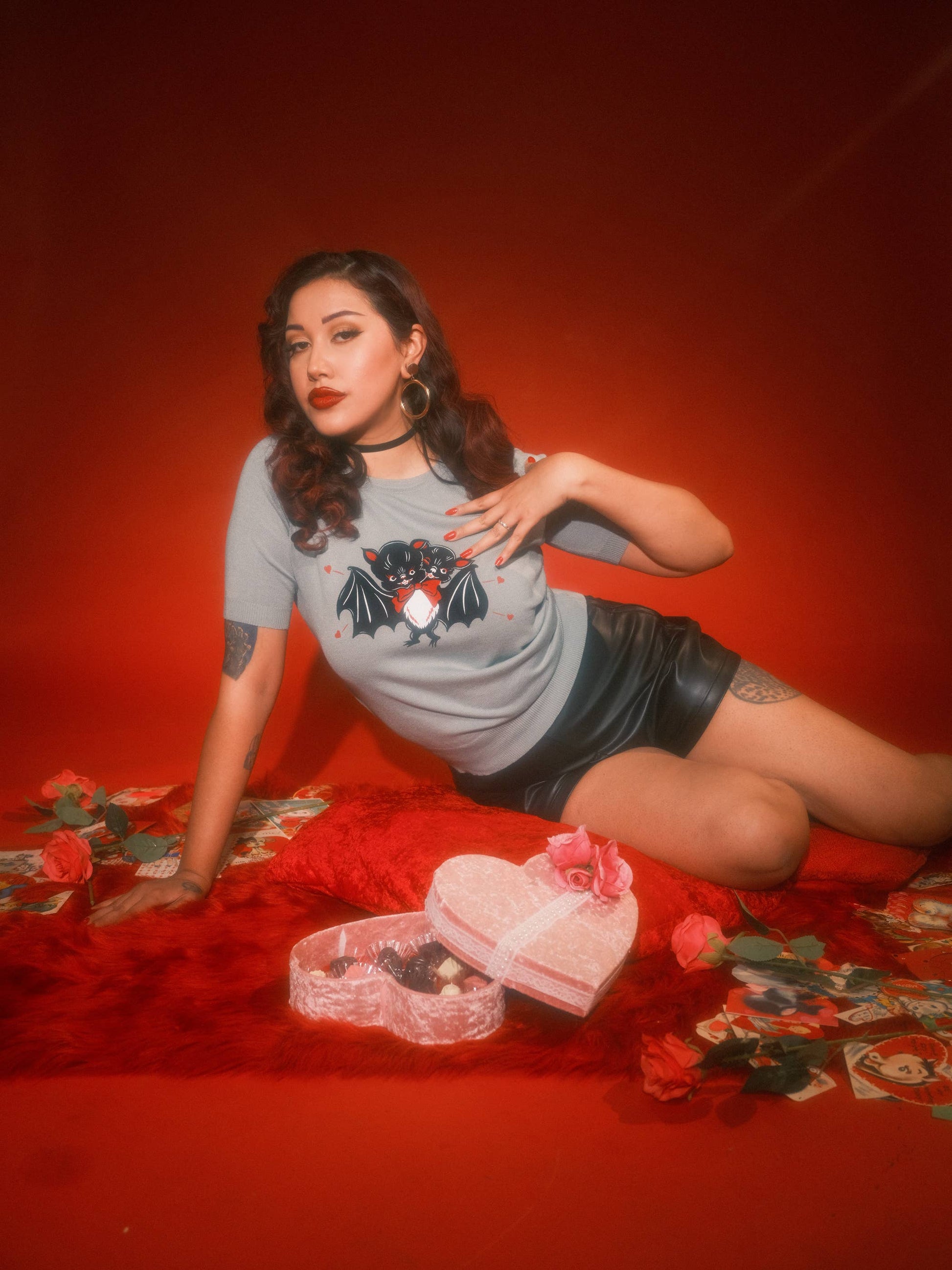 Woman wearing a graphic t-shirt sitting on a red surface with decorative elements.