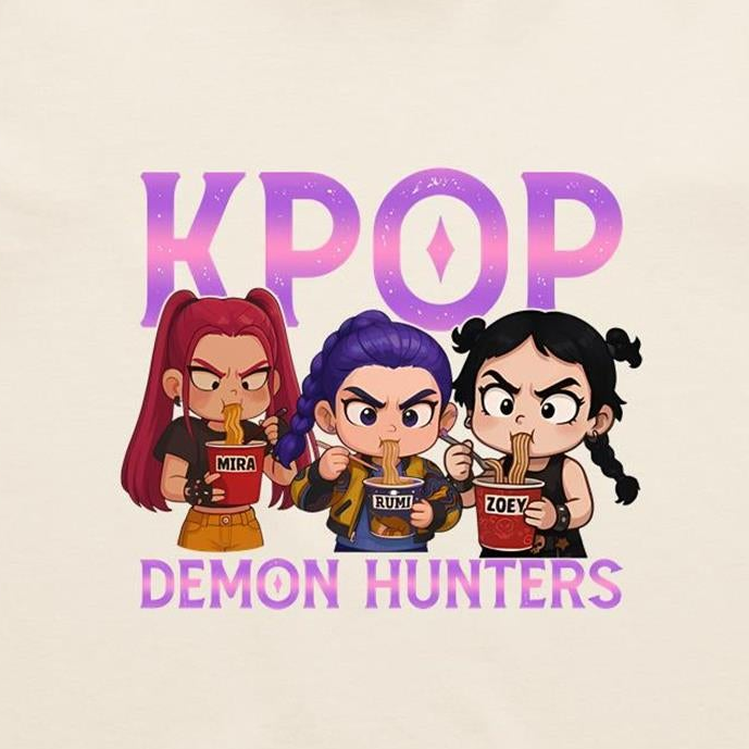 A graphic print featuring three chibi-style cartoon girls eating noodles, with the word 'K-POP' above them and 'DEMON HUNTERS' below, on a light cream background.