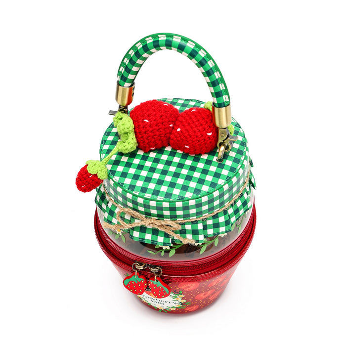 A strawberry-themed handbag designed to look like a picnic basket, featuring a green and white gingham patterned top with a crocheted red strawberry and green stem handle, and a red lower basket body with a clear front window and small hanging strawberry charms.