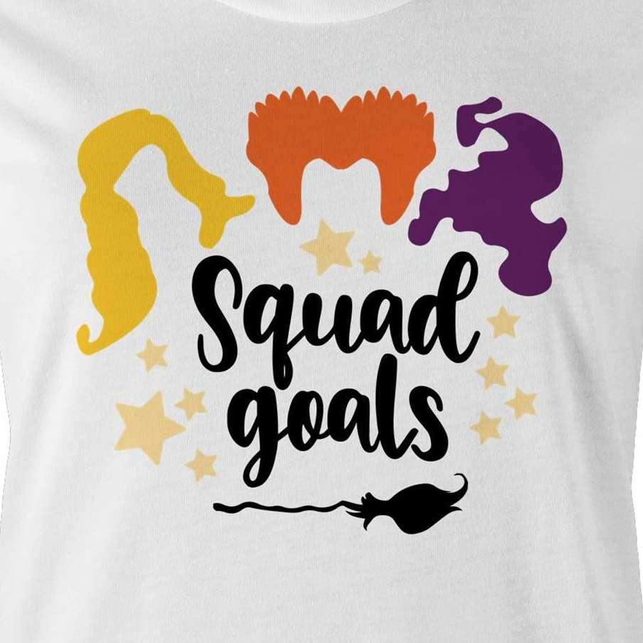 A close-up of a white graphic t-shirt featuring the text 'Squad goals' in black script, surrounded by yellow stars and stylized hair silhouettes in yellow, orange, and purple, with a black broomstick graphic below.